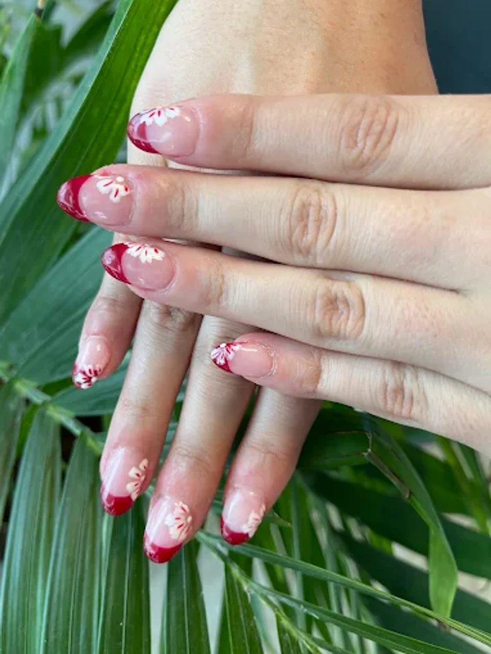 Red french tip nails with white floral accents on almond-shaped nails