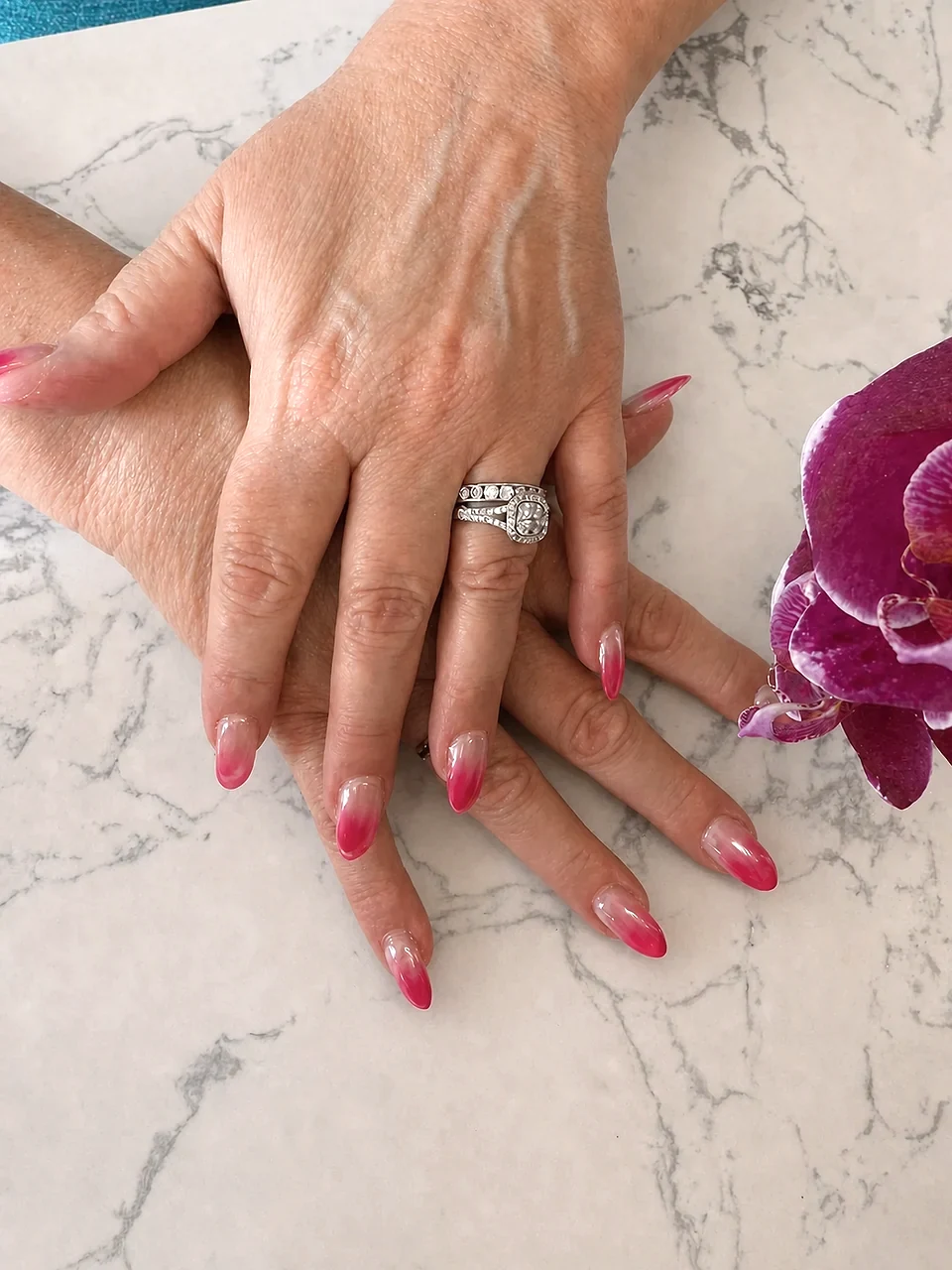 Pink ombre almond nails posed beside a purple orchid